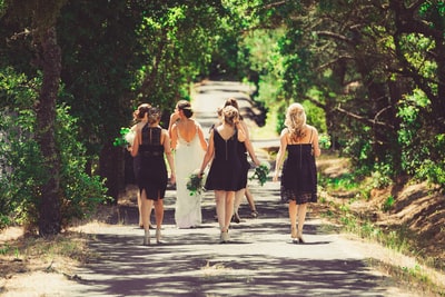 新娘和伴娘在绿树间的街道上行走